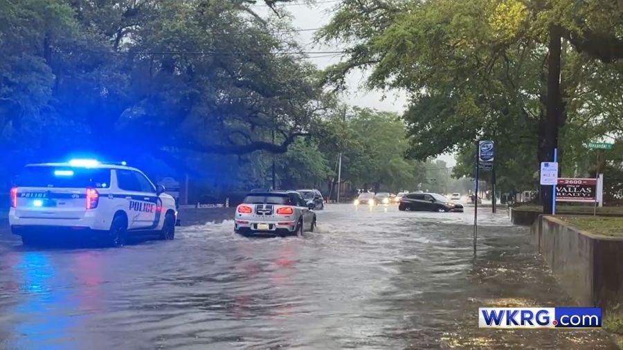 Car passes Mobile Police Department patrol vehicle in floodwater on Florida Street in Mobile, Alabama.